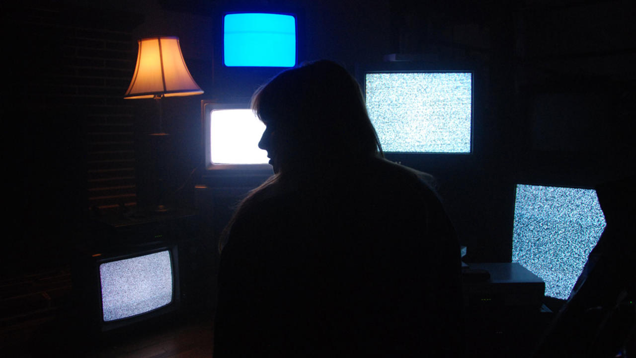 Silhouetted figure in front of five TVs of static